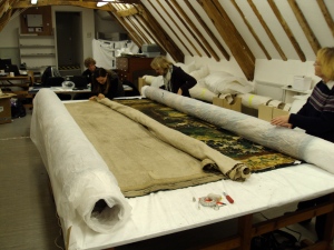 The tapestries are stored on a roller. We unroll one end, work on it, and then carefully roll it to another roller. 