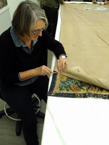 Val uses a scaple to cut the through the stitching attaching the lining to the tapestry.